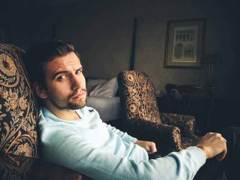 Man in hotelkamer op een luxe stoel kijkt peinzend - is hij blij of niet?