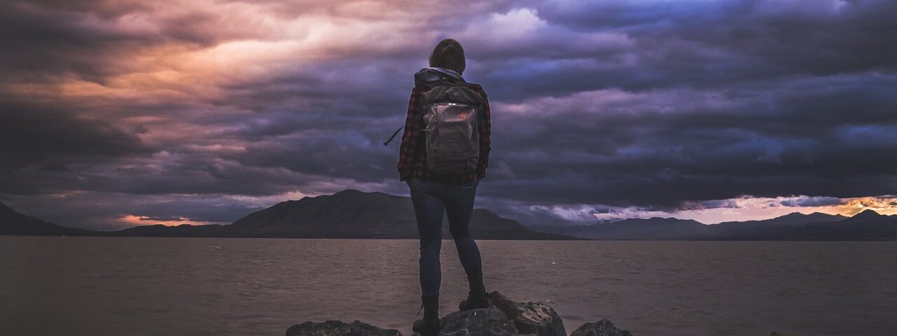 Meisje met backpack voor groot meer. donkere wolken.