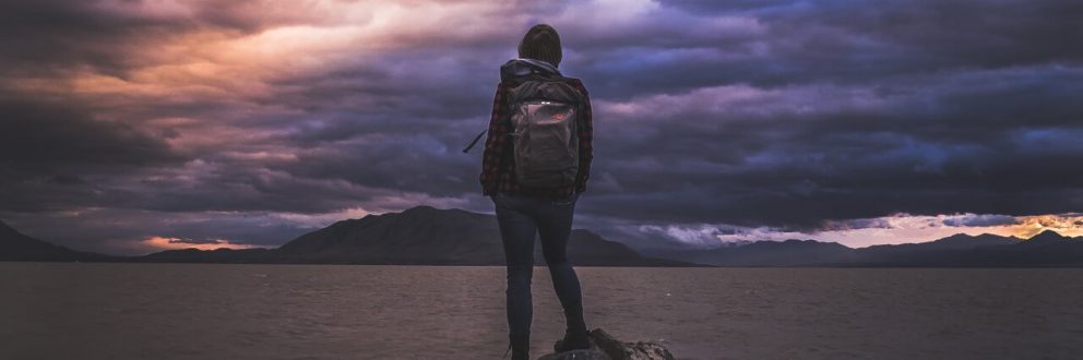 Meisje met backpack voor groot meer. donkere wolken.