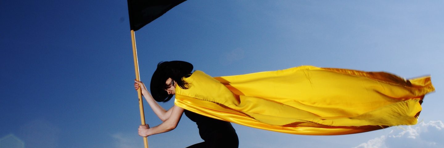 vrouw met gele cape en zwarte vlag in dramatische pose