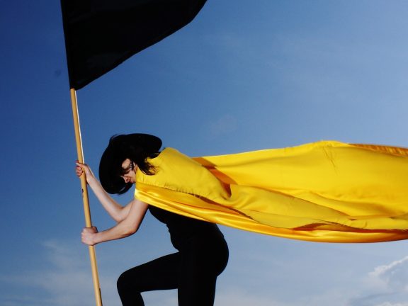 vrouw met gele cape en zwarte vlag in dramatische pose