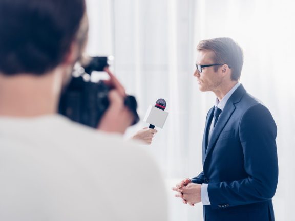 selective focus of handsome businessman in glasses giving video interview to journalist in office