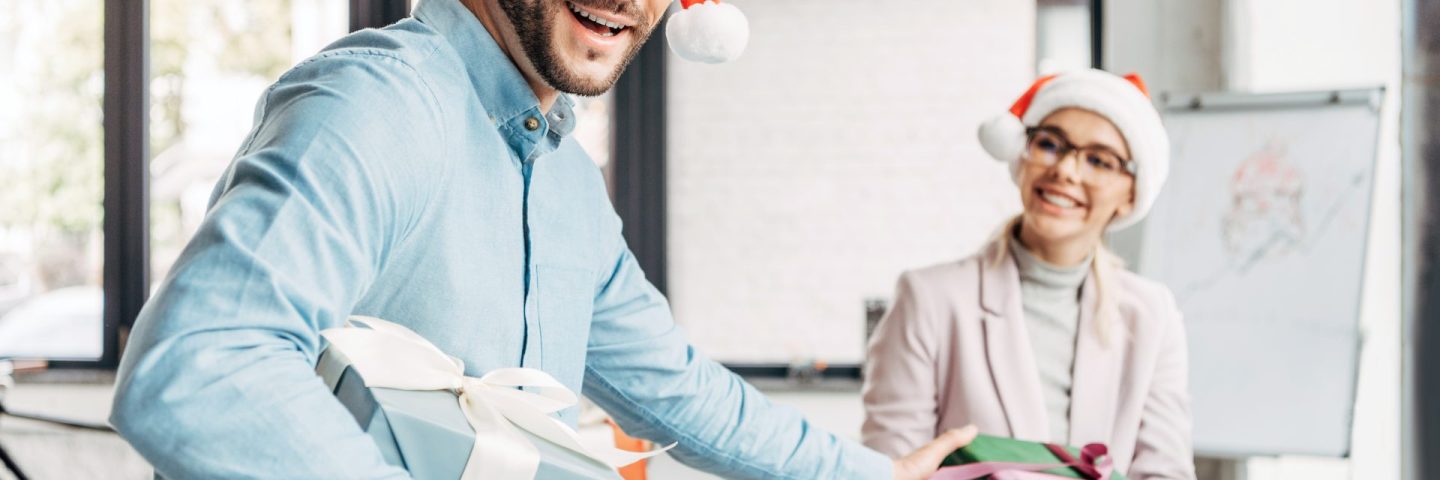 happy young businessman presenting christmas gift to female colleague in office