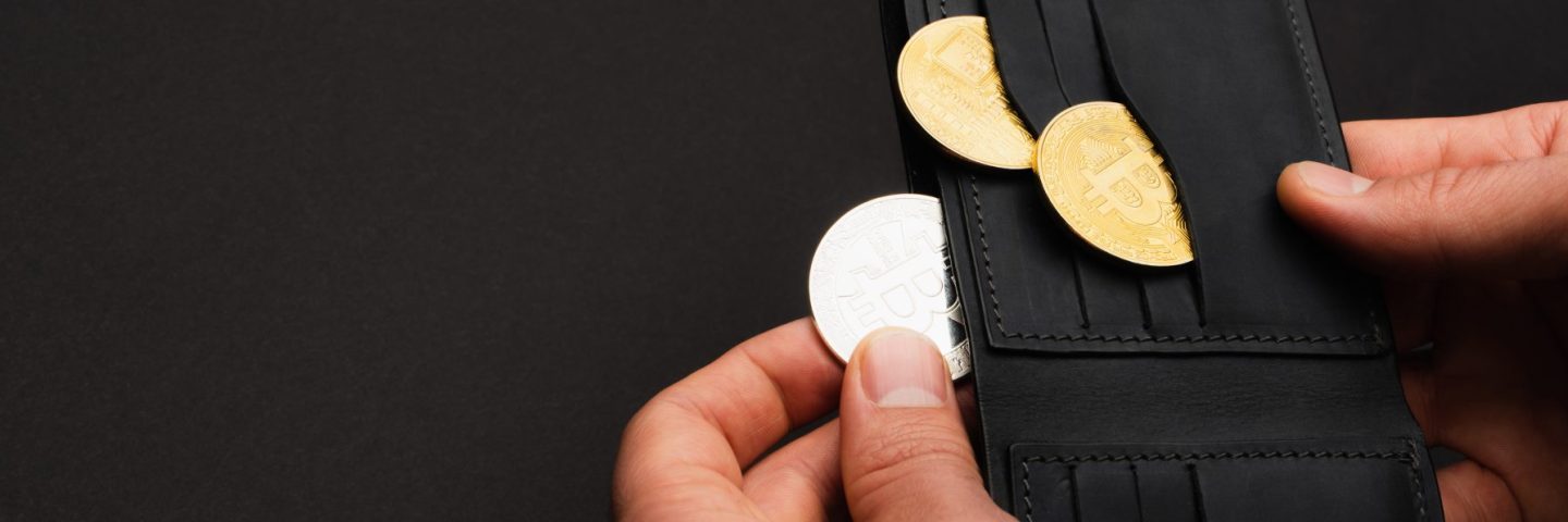 KYIV, UKRAINE - APRIL 26, 2022: Cropped view of man holding silver crypto coin and wallet isolated on black, banner