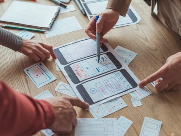 Cropped view of designers working with app sketches and template of mobile website at table