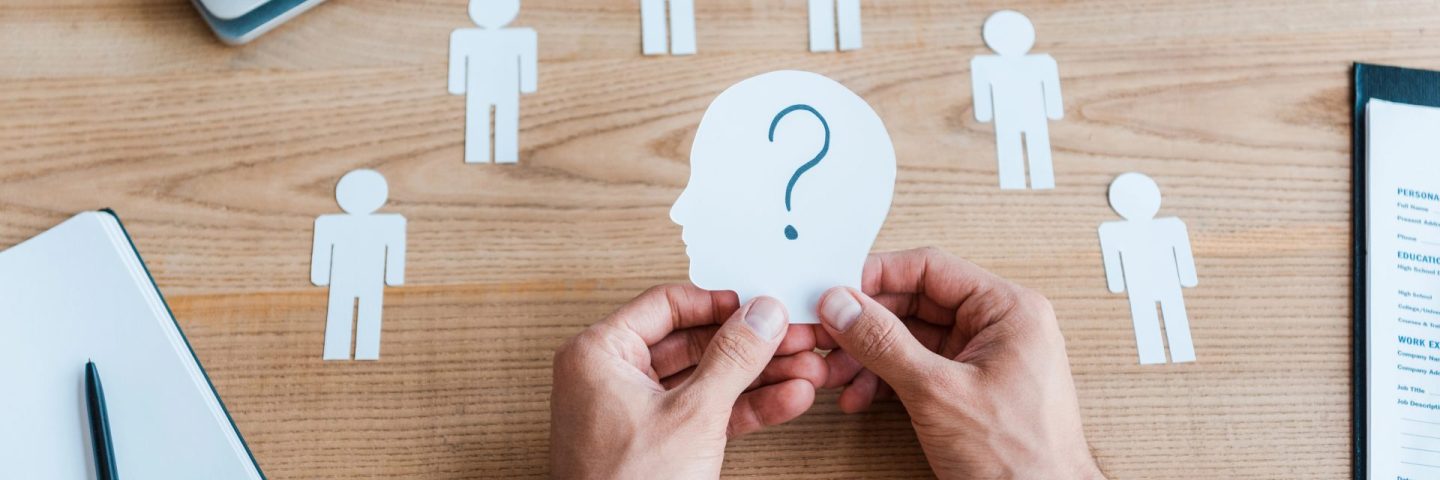 cropped view of recruiter holding paper human shape with question mark on table