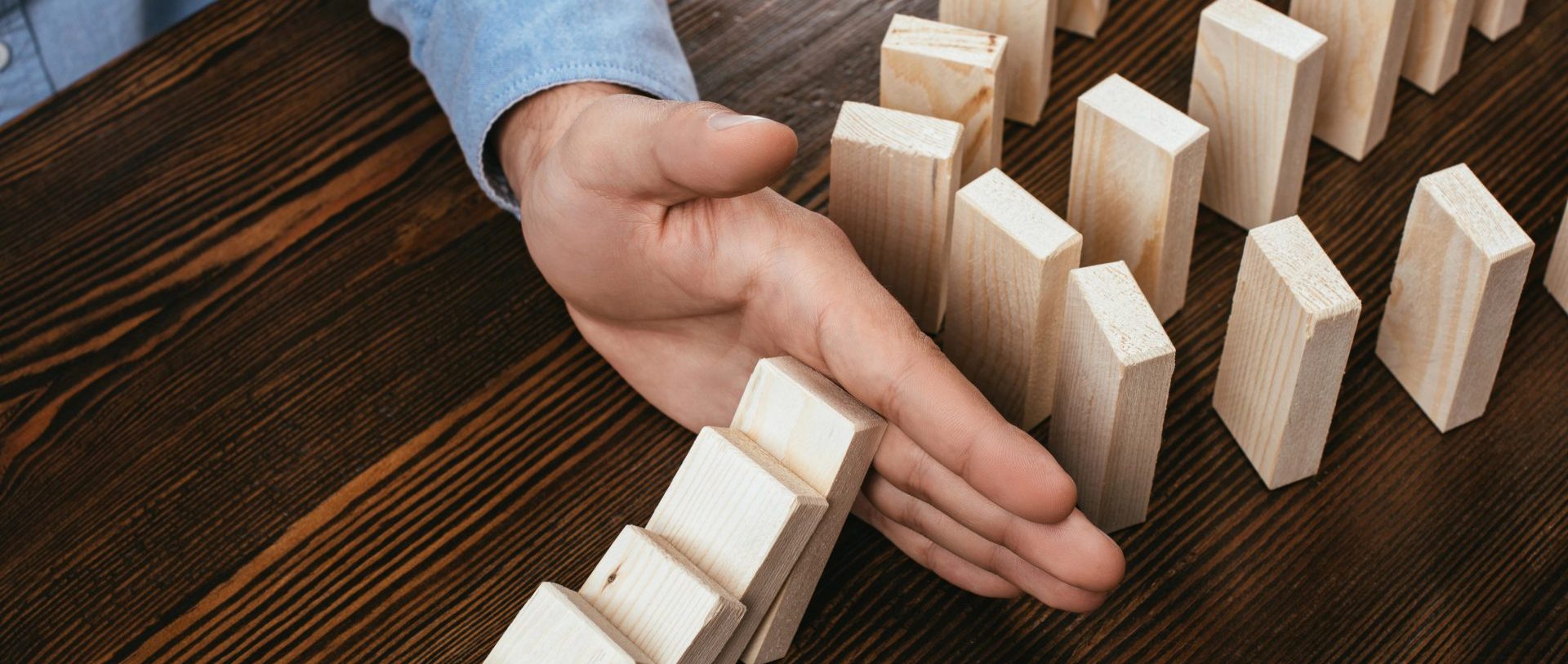 partial view of man preventing wooden blocks from falling on desk