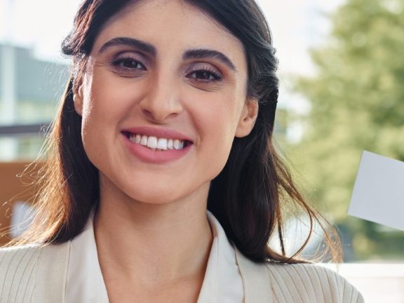 A businesswoman confidently holds a business card in her hand in a modern office setting.