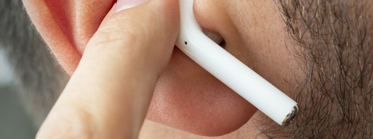 Izmir, Turkey - July  12, 2019: Close up shot of the one of Apple brand airpods on a caucasian white males ear and pushing it with forefinger.