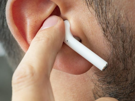 Izmir, Turkey - July  12, 2019: Close up shot of the one of Apple brand airpods on a caucasian white males ear and pushing it with forefinger.