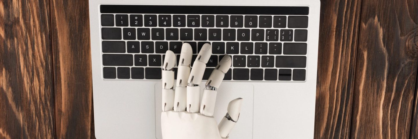 cropped shot of robot working with laptop on wooden surface