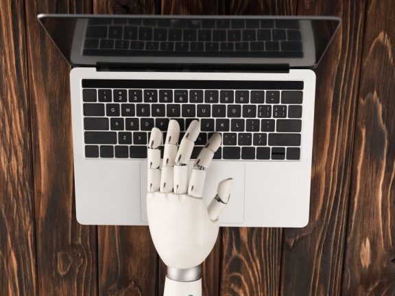 cropped shot of robot working with laptop on wooden surface