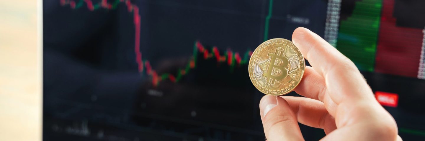 Closeup image of male hands holding golden bitcoin on background with laptop screen with financial chart data, crypto trader checking and controlling financial database on international exchanges