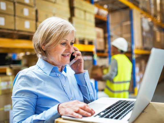 Senior woman manager with smartphone and man worker working in a warehouse.