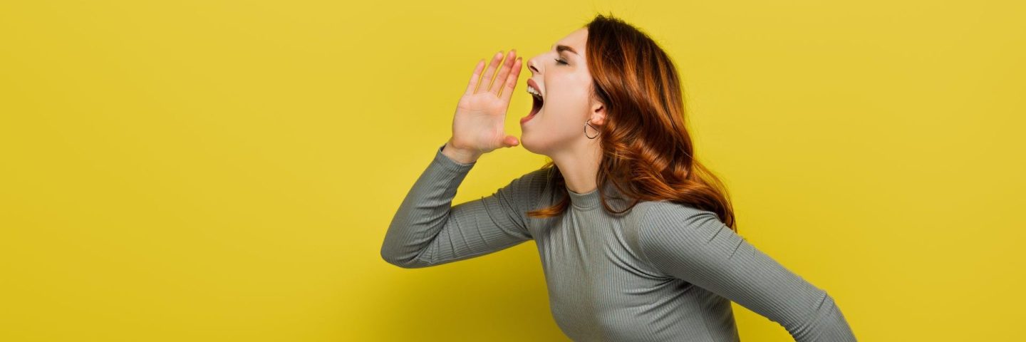 young woman with wavy hair screaming on yellow