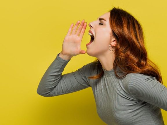 young woman with wavy hair screaming on yellow