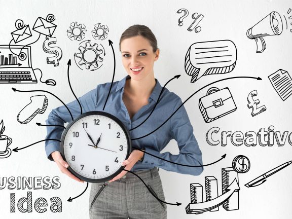 Smiling businesswoman holding wall clock in hands on white with creative business idea inscription and hand-drawn icons