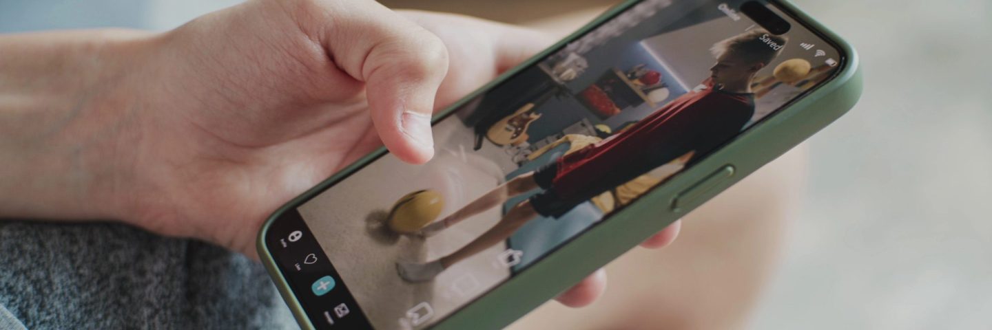 Smartphone application with various video content displayed on phone screen. Close up of teenager scrolling and watching social media feed with short videos using mobile phone while sitting on sofa.