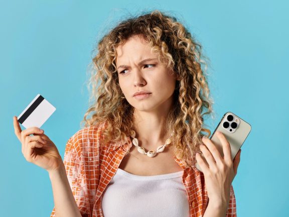 A woman with curly hair holding credit card and a cell phone.