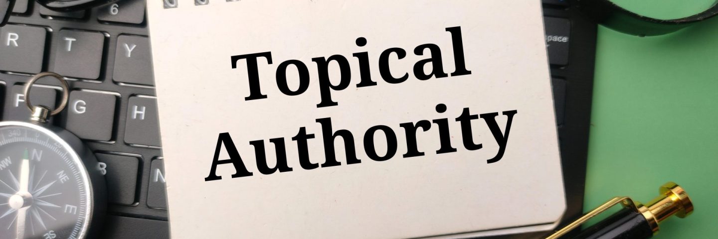 Pen and glasses with the word Topical Authority on a black keyboard and green background.