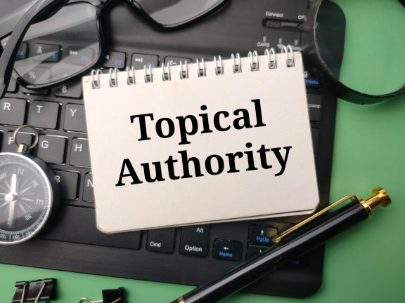 Pen and glasses with the word Topical Authority on a black keyboard and green background.