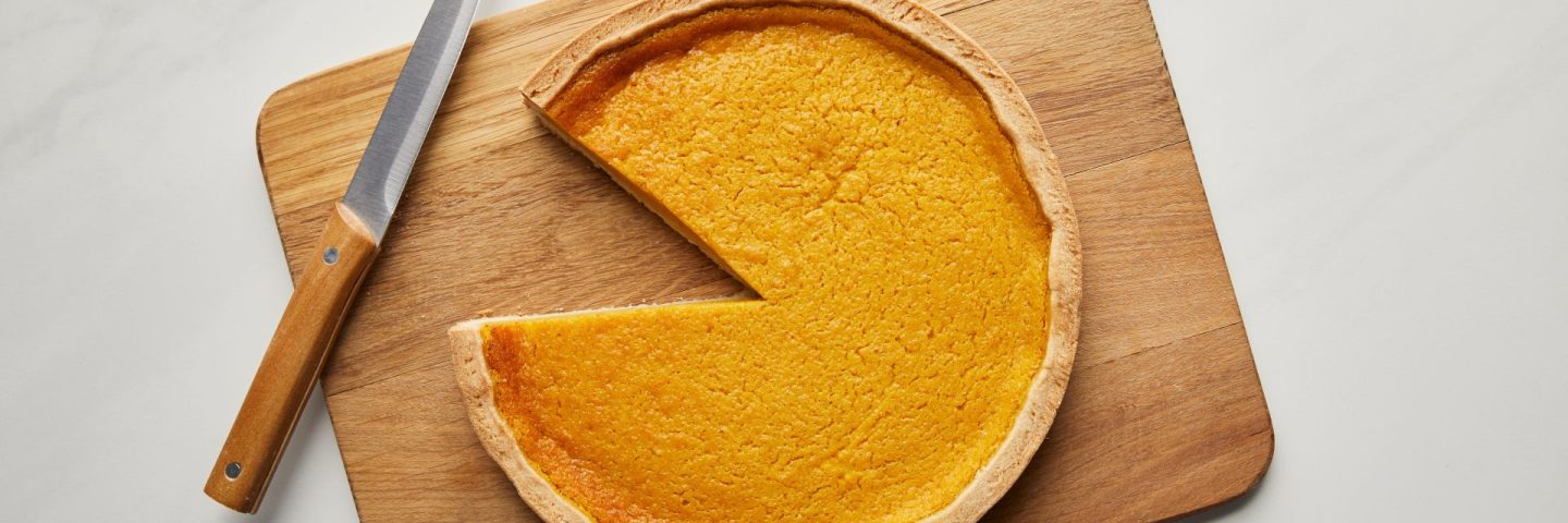 top view of cut pumpkin pie on chopping board near knife on white marble surface