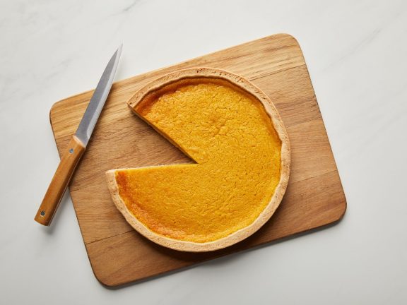 top view of cut pumpkin pie on chopping board near knife on white marble surface