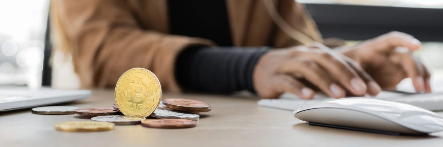 KYIV, UKRAINE - APRIL 27, 2022: Cropped view of bitcoins near blurred african american businesswoman typing on computer keyboard