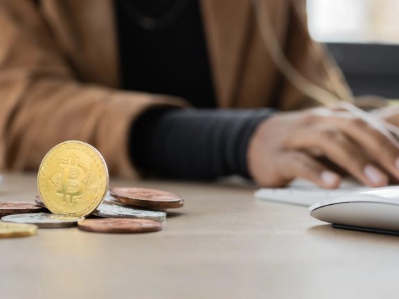 KYIV, UKRAINE - APRIL 27, 2022: Cropped view of bitcoins near blurred african american businesswoman typing on computer keyboard