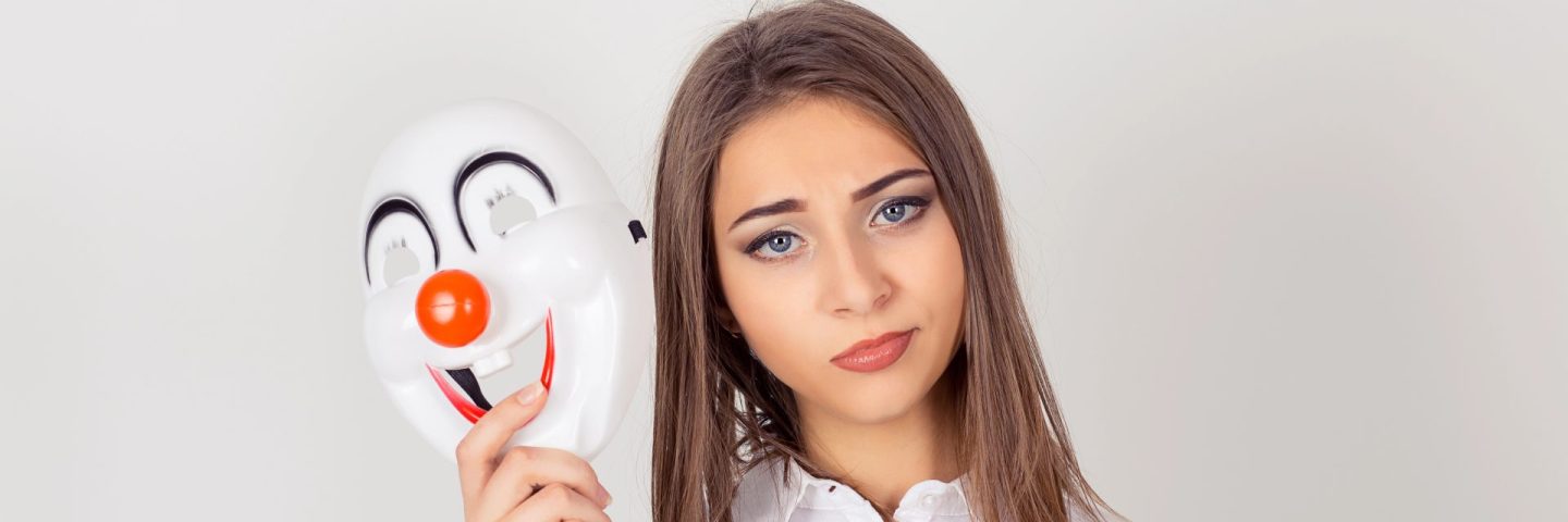Doubtful inside. Wearing a mask. Portrait young doubtful worried woman with skeptical expression holding a clown mask expressing cheerfulness happiness looking at camera isolated white background.