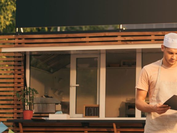 handsome chef in apron looking at clipboard near food truck