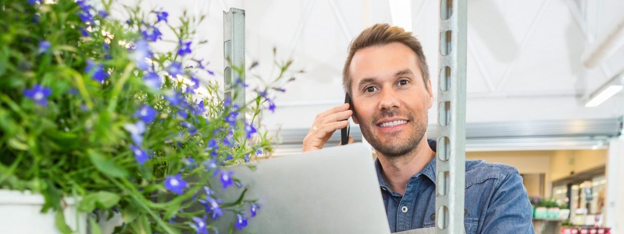 Florist Using Mobile Phone And Laptop In Shop