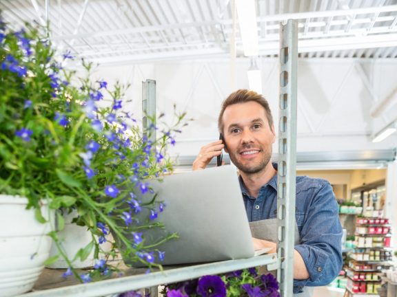 Florist Using Mobile Phone And Laptop In Shop