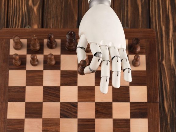 cropped shot of robot playing chess with human on wooden surface