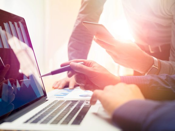 Two colleagues working on new global financial strategy plan using laptop and smartphone.Modern business team innovation concept.Project meeting at office with virtual graph and chart data interface