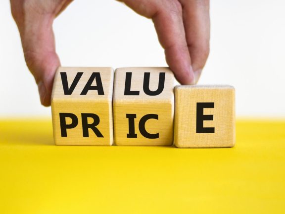 Value and price symbol. Businessman turns wooden cubes and changes the word price to value or vice versa. Beautiful yellow table, white background, copy space. Business value and price concept.