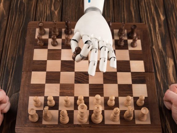 cropped shot of robot playing chess with human on wooden tabletop