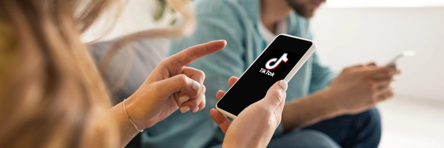 KYIV, UKRAINE - FEBRUARY 21, 2020: Selective focus of woman pointing with finger at smartphone with TikTok app near boyfriend chatting on couch