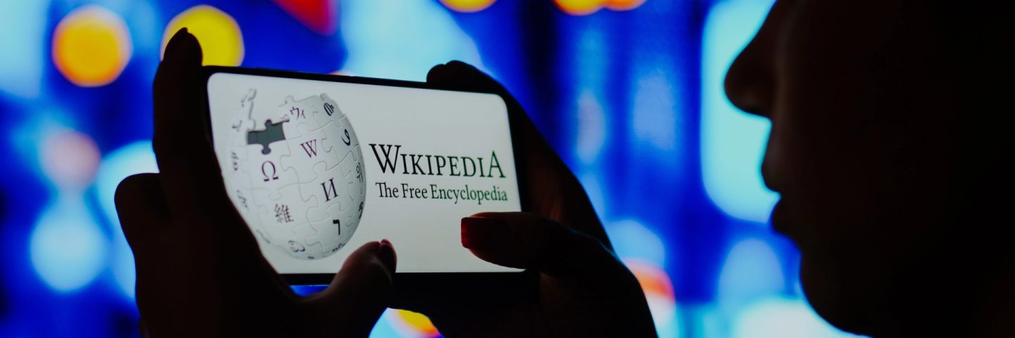 June 6, 2022, Brazil. In this photo illustration, a silhouetted woman holds a smartphone with the Wikipedia logo displayed on the screen