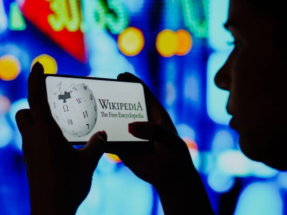 June 6, 2022, Brazil. In this photo illustration, a silhouetted woman holds a smartphone with the Wikipedia logo displayed on the screen