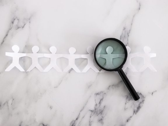 staff shortages and hiring personnel conceptual image, paper people chain with magnifying glass analysing them