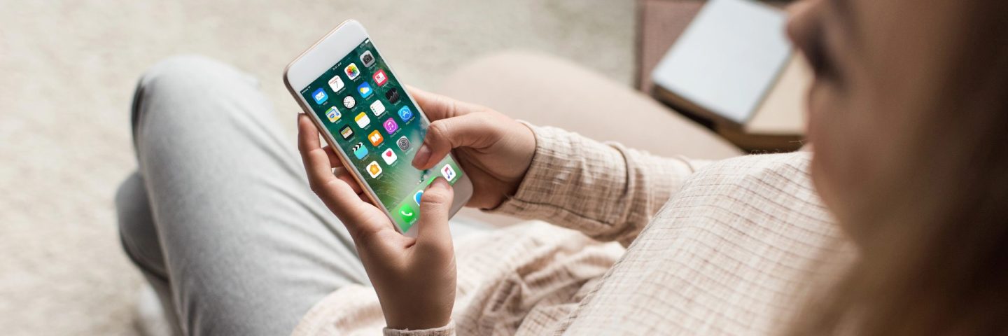 cropped shot of woman on couch using smartphone with ios apps on screen