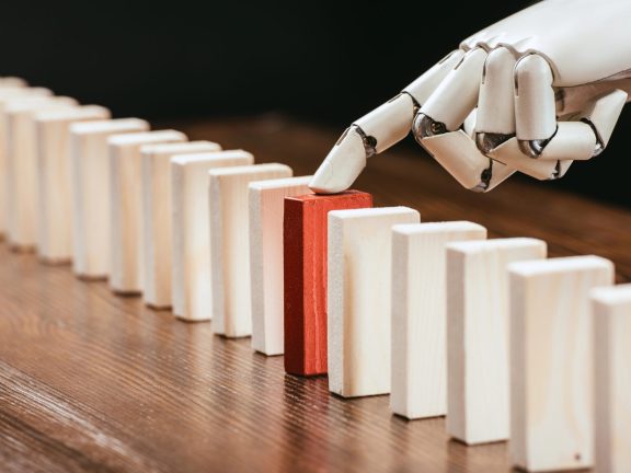 selective focus of robotic hand picking red wooden brick from row of blocks on desk