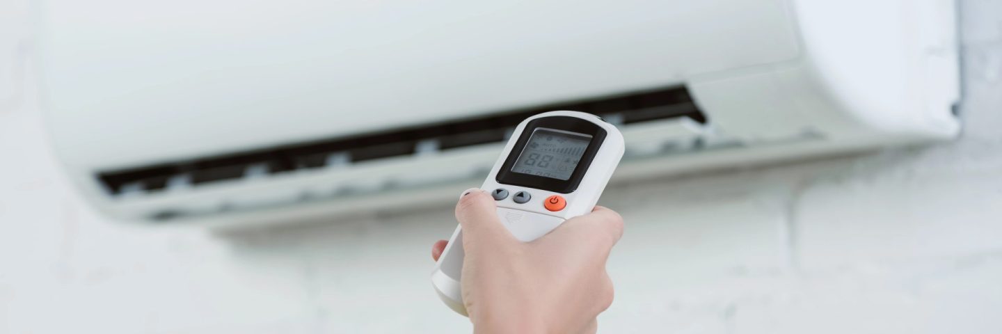 cropped shot of woman pointing at air conditioner hanging on brick wall with remote control