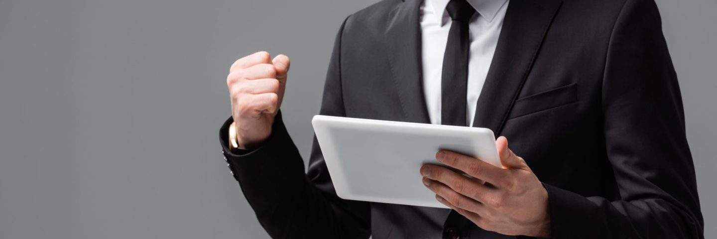 partial view of successful businessman with digital tablet showing win gesture isolated on grey