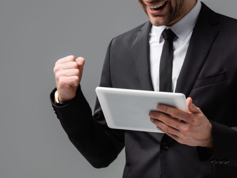 partial view of successful businessman with digital tablet showing win gesture isolated on grey