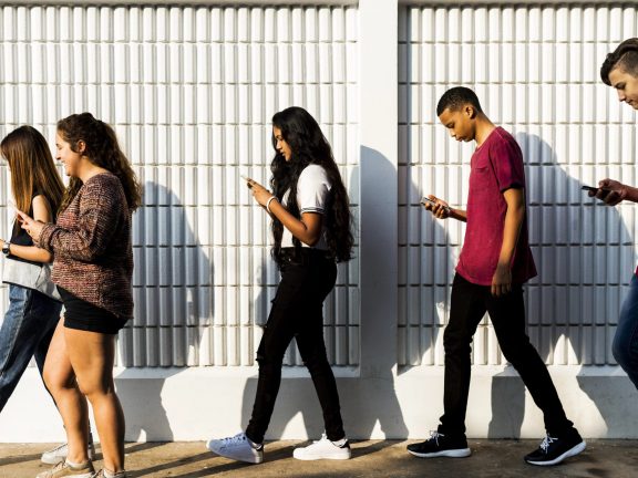 Group of young teenager friends walking home after school using smartphones addiction concept