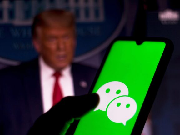 September 28, 2020, Brazil. In this photo illustration a WeChat logo is seen displayed on a smartphone. President Donald Trump appears in the background. App is banned in the United States