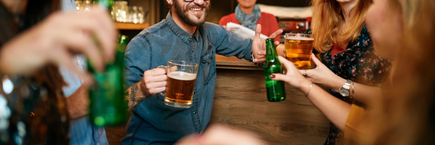Small group of people standing at pub, chatting, drinking beer and enjoying friday night. Night out.