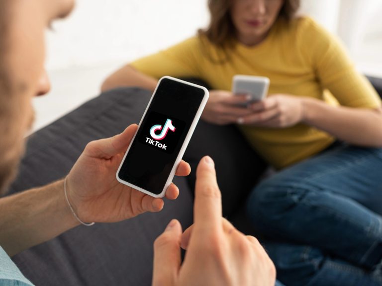 KYIV, UKRAINE - FEBRUARY 21, 2020: Selective focus of man holding smartphone with TikTok app near woman at home